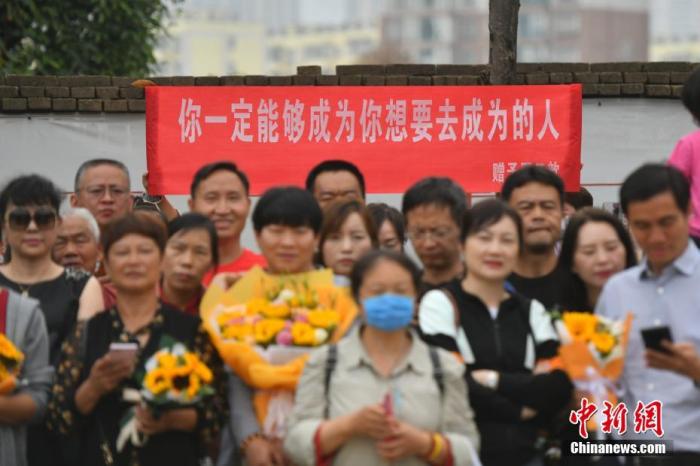 资料图：6月8日，云南省昆明市的考生结束2021年全国高考。图为考试结束后，一幅助考标语前有考生和家长合影留念。 中新社记者 刘冉阳 摄 